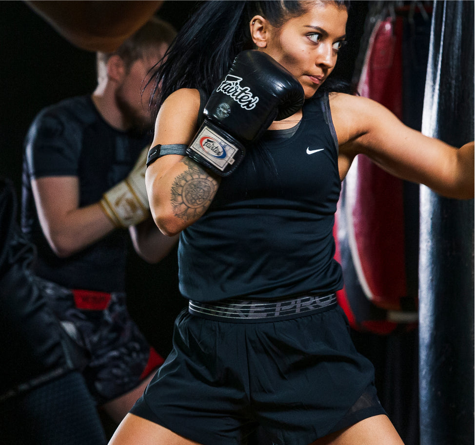 A woman wearing an upper arm heart rate monitor boxing in a gym.