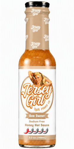 A bottle of Jersey Girl Honey Hot Sauce, 'Bee Sweet' variety, featuring a white label with a retro pin-up illustration and orange lettering, set against a plain white background.